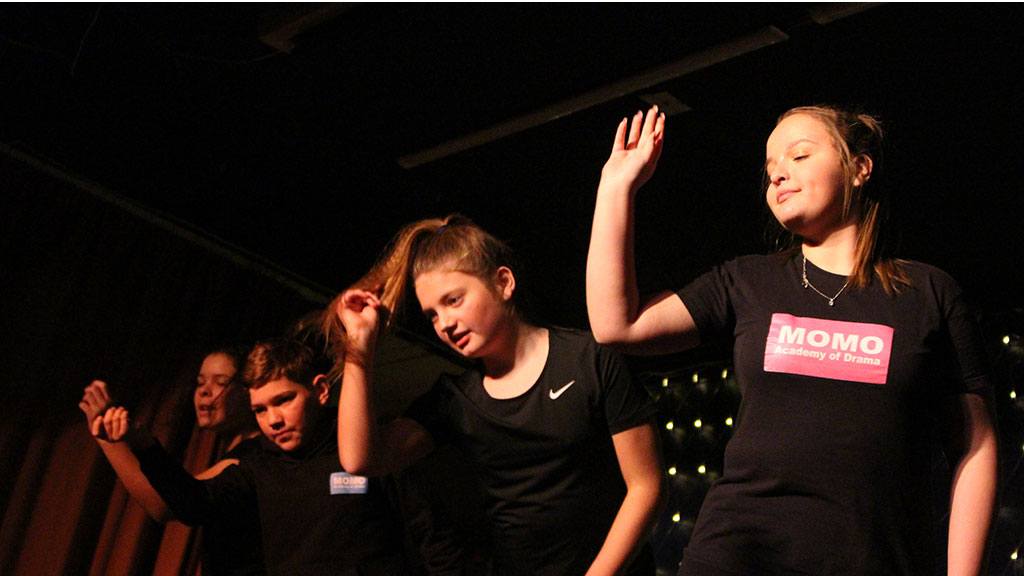 MOMO Academy of Drama group performing raising their arms and leaning forward